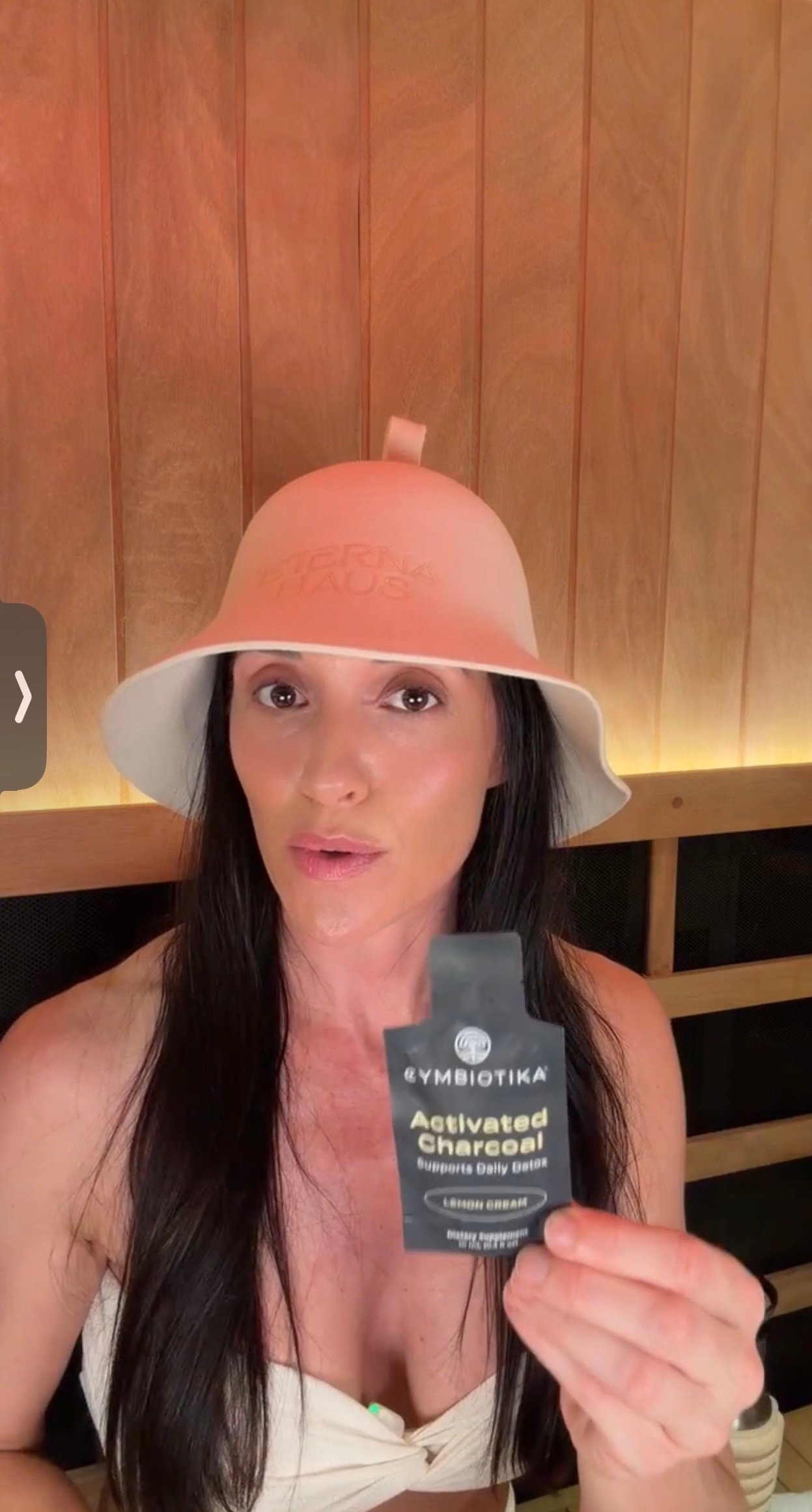 Wearing the ETERNA HAUS Merino Wool Sauna Hat while holding an activated charcoal binder packet