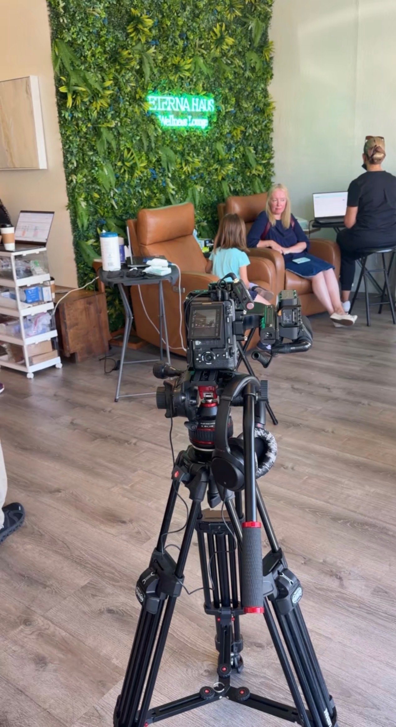 Behind the scenes of a filming day at ETERNA HAUS with professional cameras on tripods facing guests in the wellness lounge recliners by the living green wall